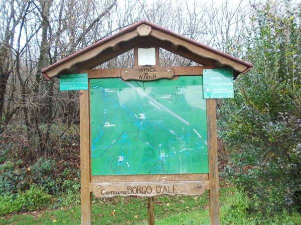 Wooden sign with green trail map at Borgo d'Ale