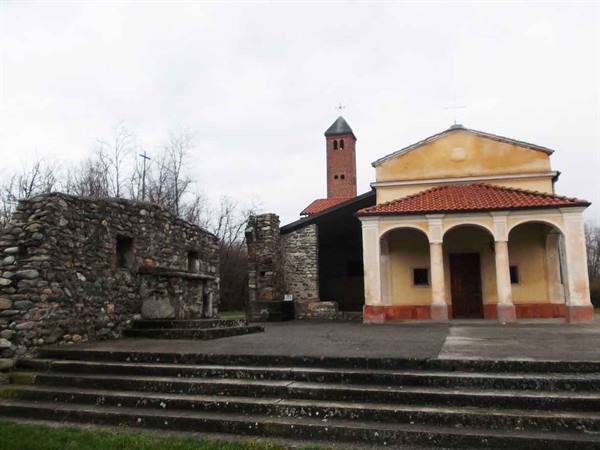 Church with arched portico and brick bell tower beside stone ruins