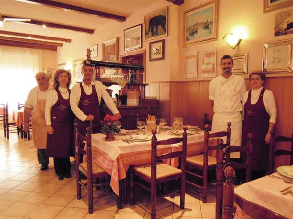Five staff in aprons beside a set table in a cozy trattoria