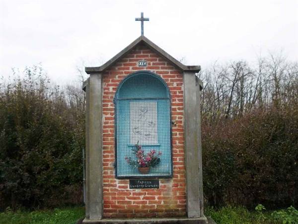 Brick wayside shrine with cross, blue painted niche, station XIV, among bushes