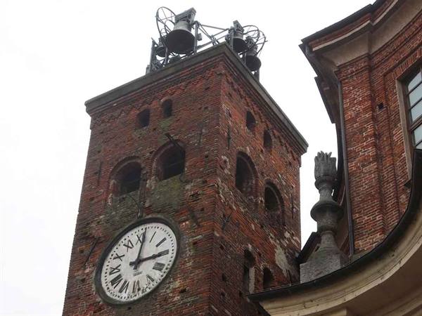 Brick clock tower with metal bell cage beside a baroque palace