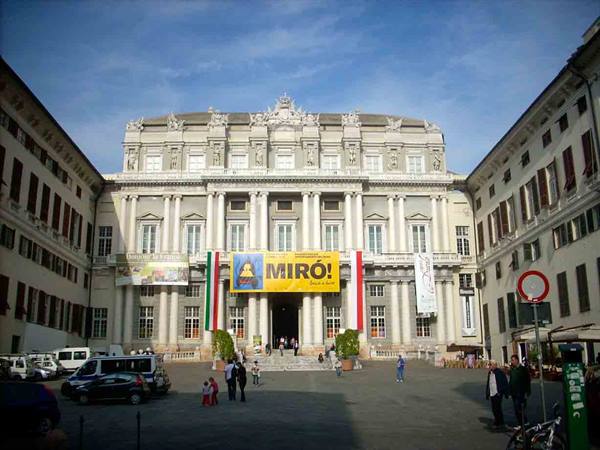 Palazzo Ducale in Genoa, bright facade with Miró exhibition banners, people in square
