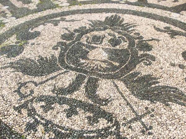 Pebble mosaic in white and black stones with grotesque mask, soft daylight