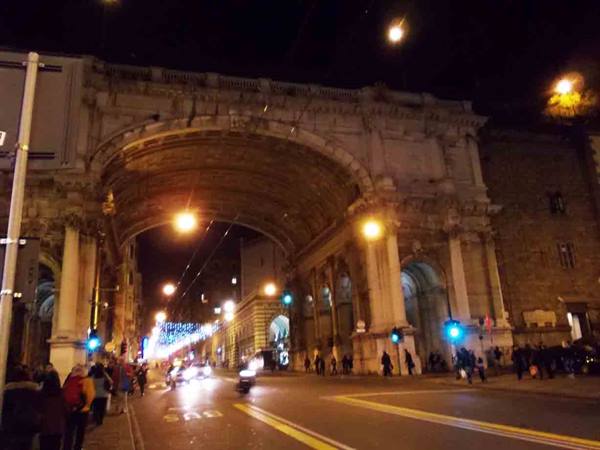 Illuminated stone arch in Florence at night, pedestrians and green traffic lights