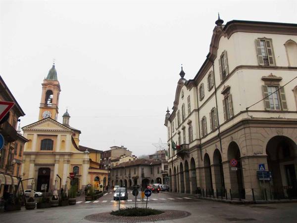 Square with yellow church and bell tower, arcades and stucco building, gray sky