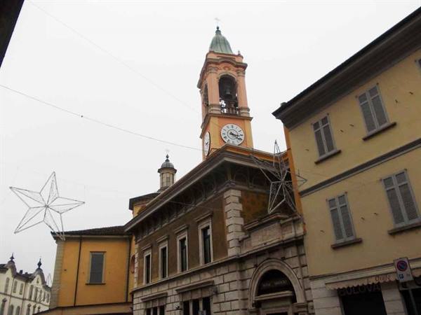Bell tower with clock among ochre buildings, Christmas star lights, grey sky