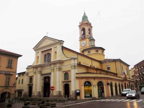 Yellow church with bell tower and clock on wet street, cars passing