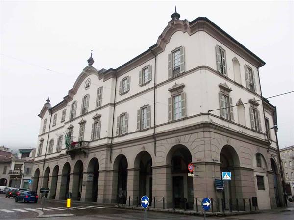 White building with arched stone arcades and shuttered windows under grey sky