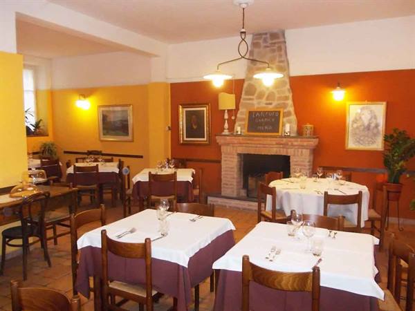 Trattoria dining room with white-clothed tables set for dinner and brick fireplace