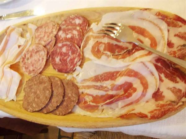 Wooden platter with salami, bacon and coppa slices, fork resting on top