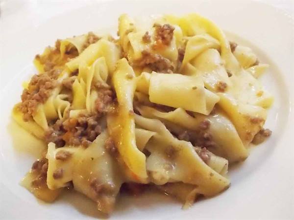 Pappardelle with meat ragù on white plate, warm close-up light