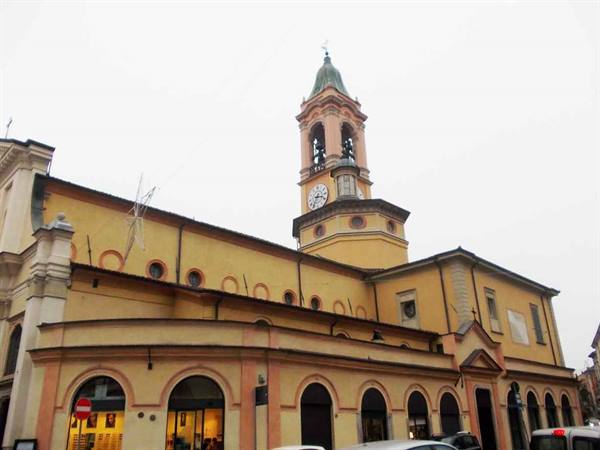 Yellow church with arched arcades and a clock bell tower under gray sky