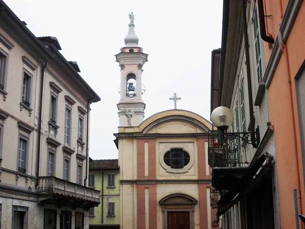 Small baroque church with bell tower among colorful buildings, gray sky