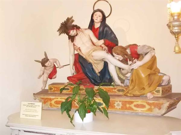 Plaster Pietà statue with angel, on a table with sign and plant