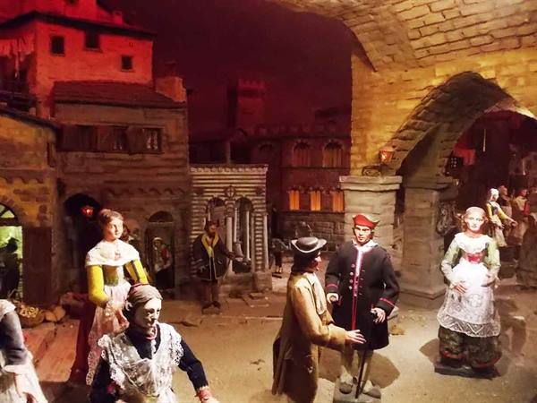 Costumed figures among stone houses and brick arches, red lighting