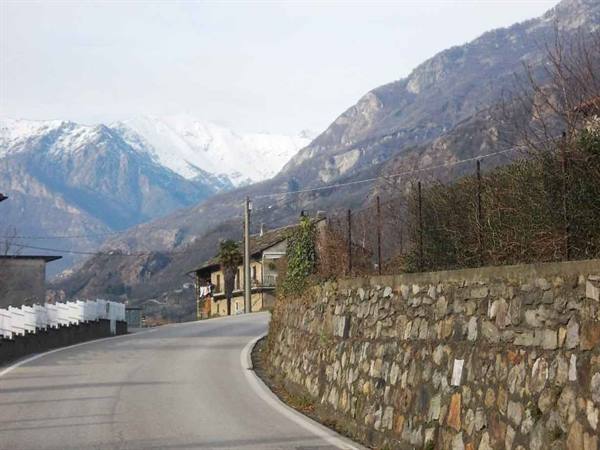 Mountain road with dry stone wall and houses beneath snowy peaks