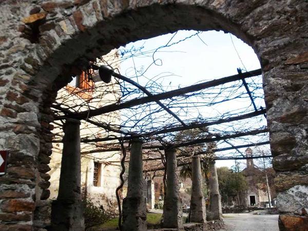 Stone arch framing a wooden pergola with vines, old village beyond
