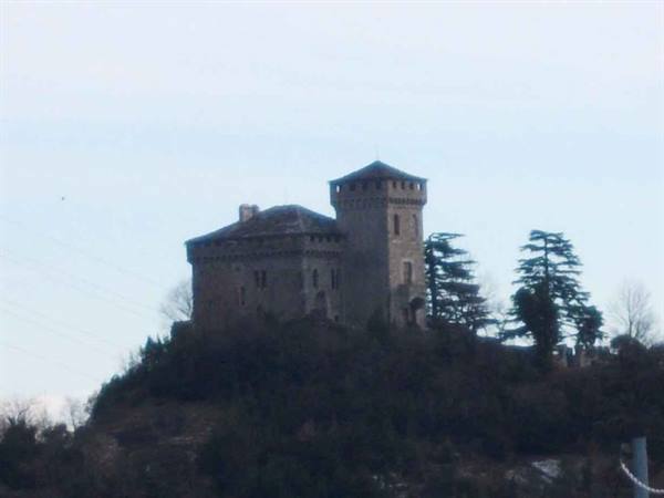 Stone castle with crenellated tower on wooded hill, gray sky