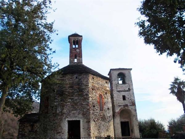 Romanesque stone church with two bell towers, framed by trees and blue sky