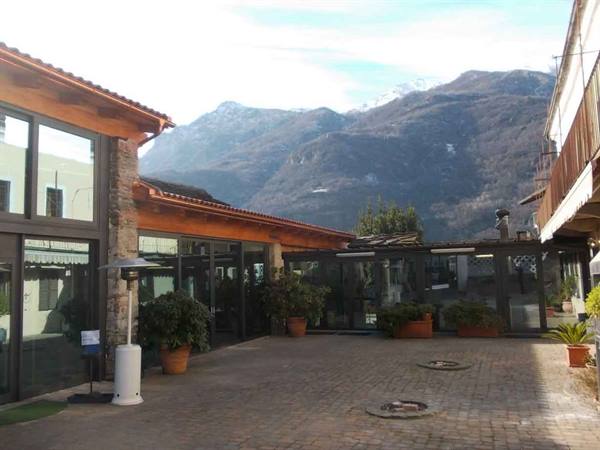 Paved courtyard with glass veranda, potted plants and snowy mountains behind