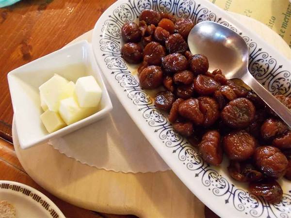 Syrup-glazed chestnuts on a decorated plate with cheese cubes and silver spoon