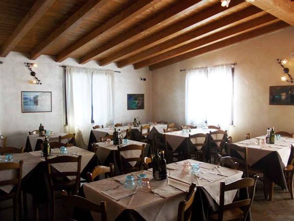 Trattoria dining room with set tables, wooden beams, light through curtains