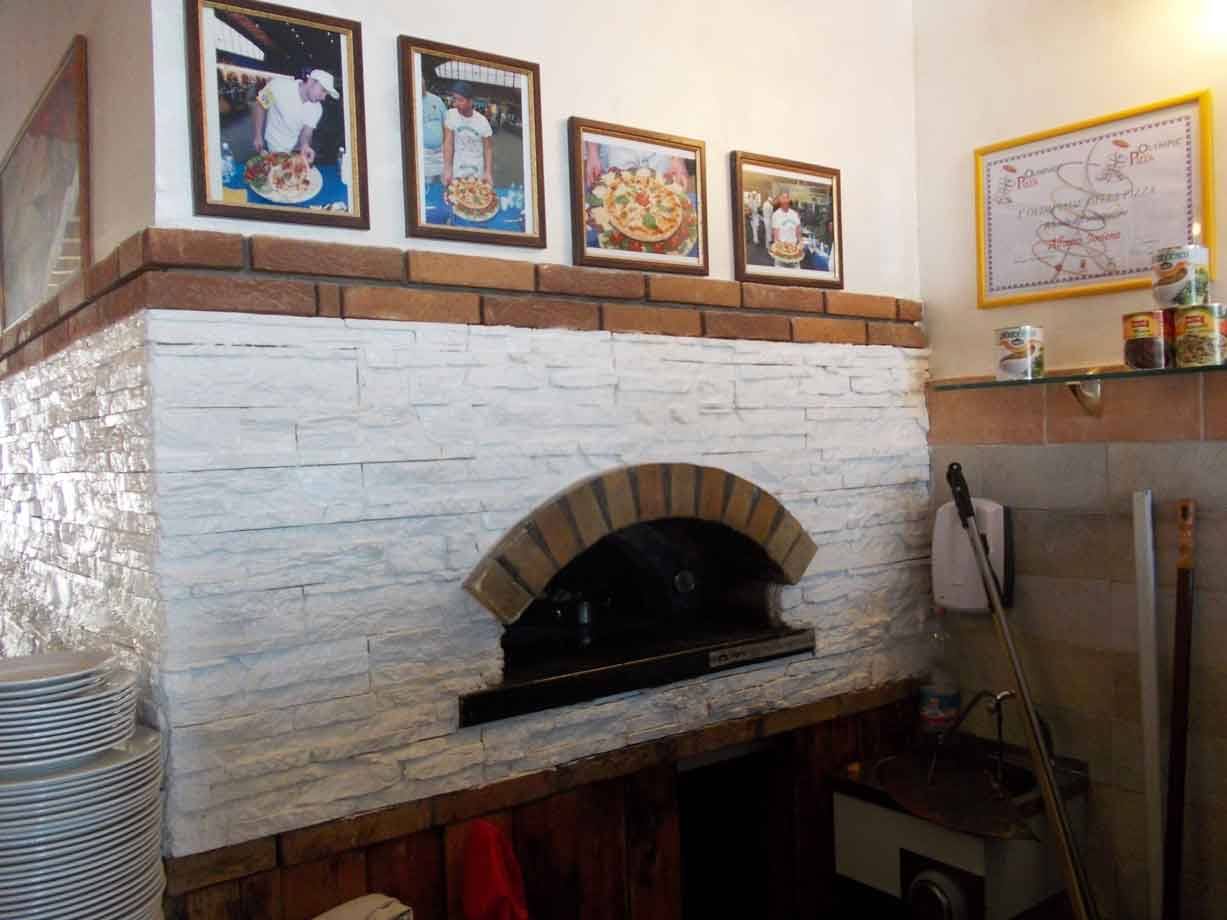 Forno a legna in muratura bianca in pizzeria, foto incorniciate sopra