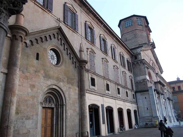 Romanesque stone facade with arched portal and rose window, side tower, people in square