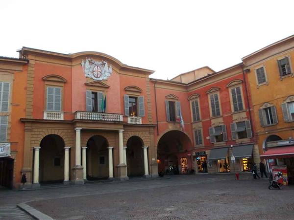 Orange building with columns and arches overlooking the square, flags at windows