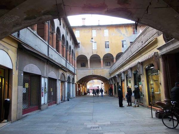 Medieval Bologna portico with brick arches, pedestrians and a bicycle