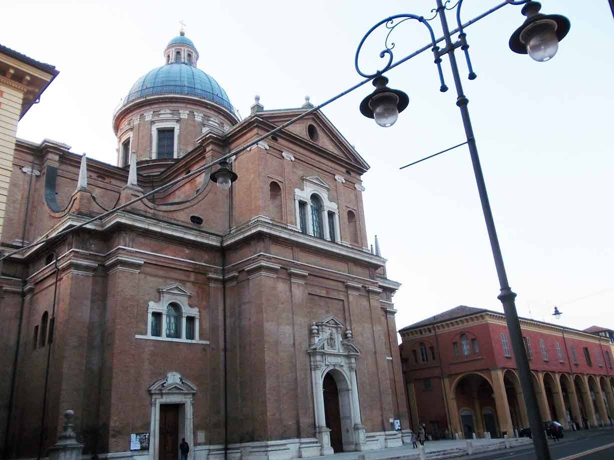 Chiesa in mattoni con cupola grigia e portali marmorei, lampioni in ferro, cielo chiaro
