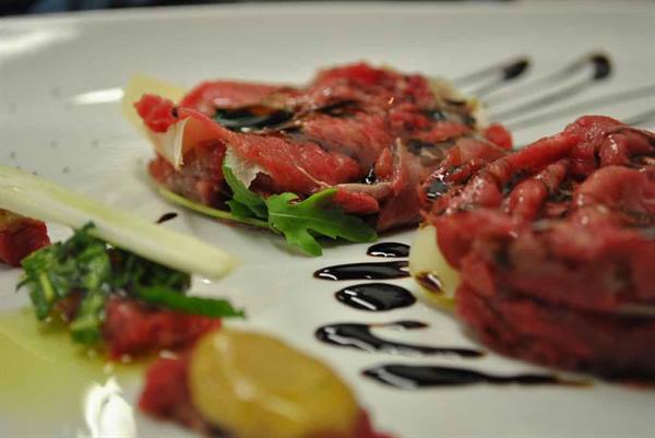 Beef carpaccio with arugula and parmesan shavings, white plate decorated with balsamic drizzle