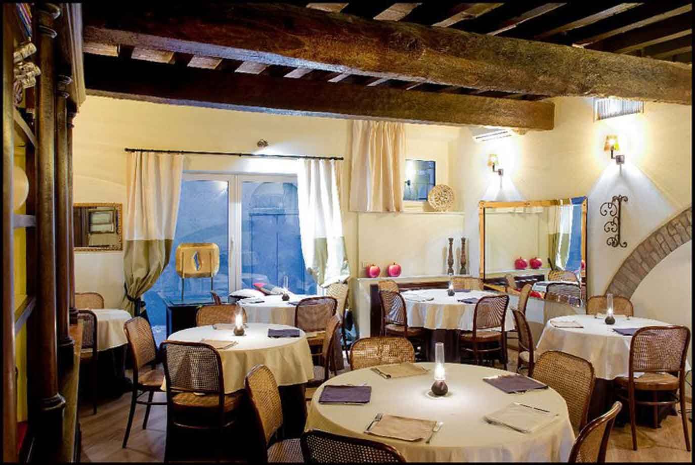 Sala di ristorante con tavoli apparecchiati, sedie di vimini e travi in legno