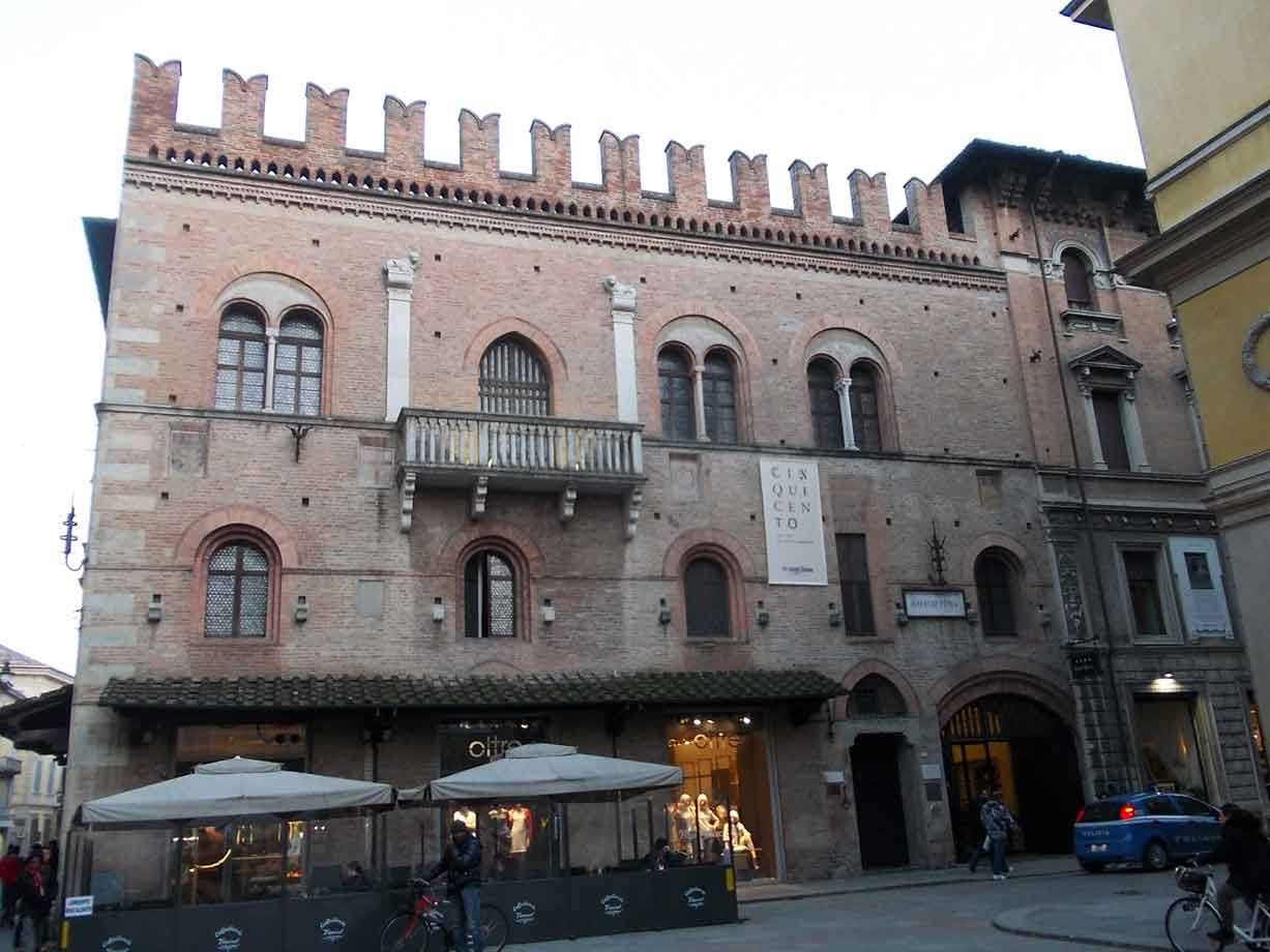 Palazzo medievale in mattoni con merlature e bifore, caffè sotto ai portici