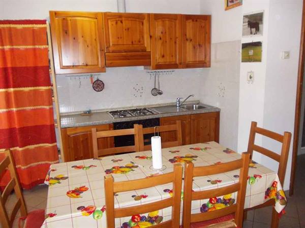 Kitchen with pine wood cabinets, table set with colorful fruit tablecloth and chairs