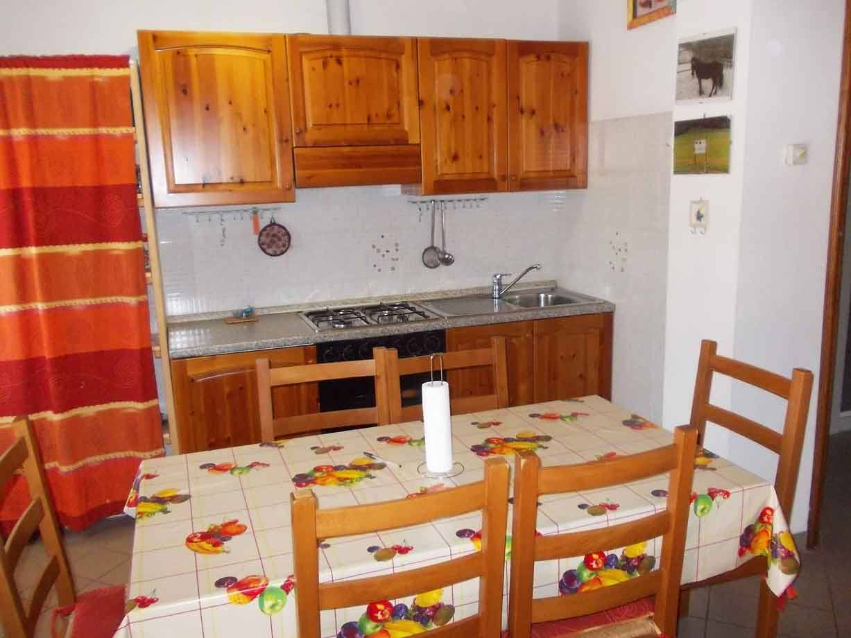 Cucina con mobili in legno di pino, tavolo apparecchiato con tovaglia colorata e sedie