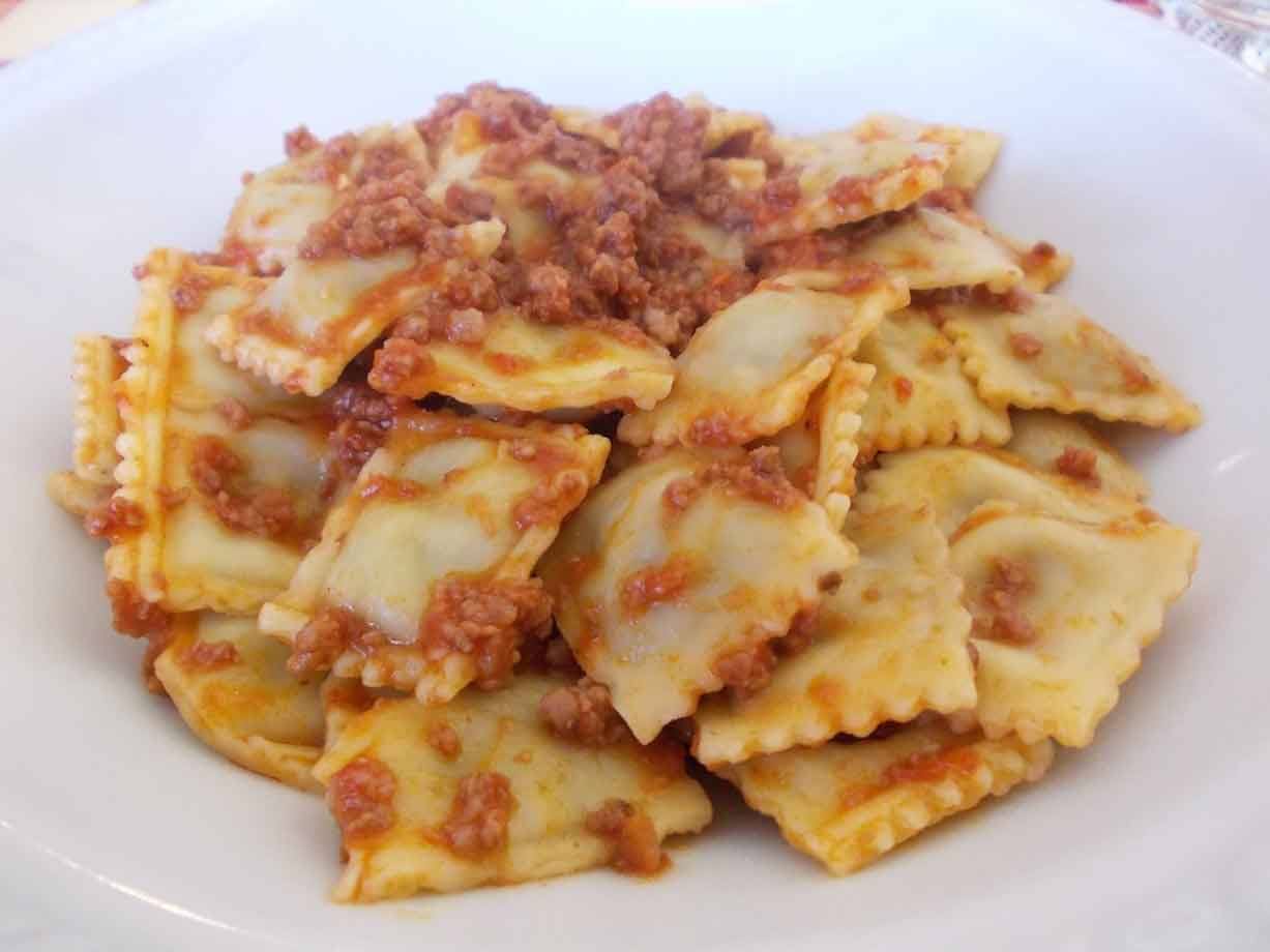 Piatto bianco con ravioli di carne al sugo, luce naturale del giorno