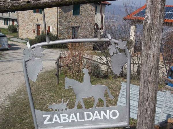 Metal sign with horseman and dog reading Zabaldano, in front of stone houses