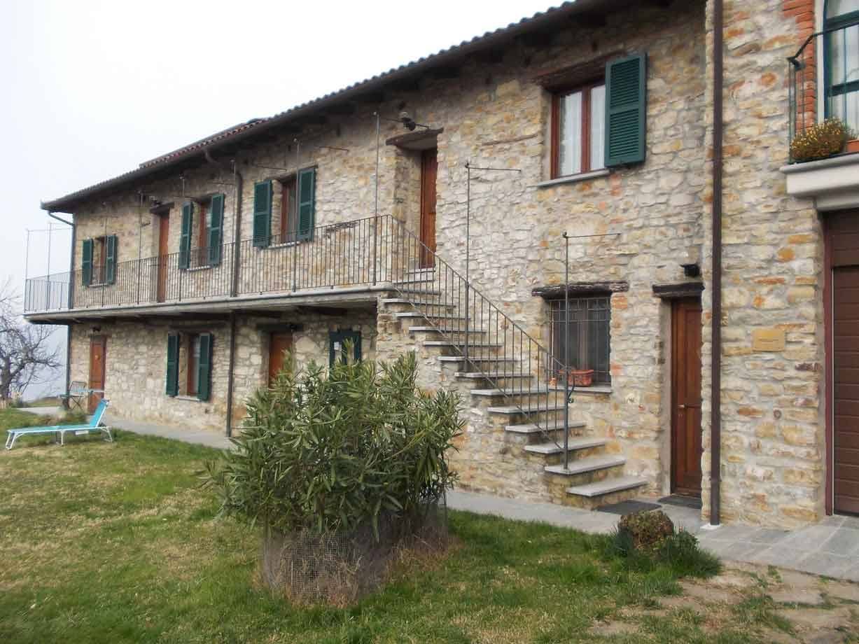 Casa rurale in pietra con persiane verdi, scala esterna in cemento e prato