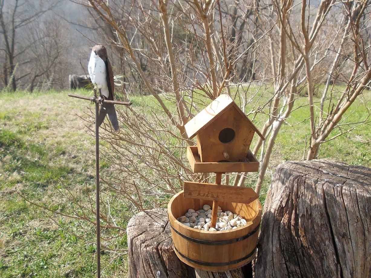 Casetta per uccelli in legno su ceppo, con statua di uccello e prato invernale