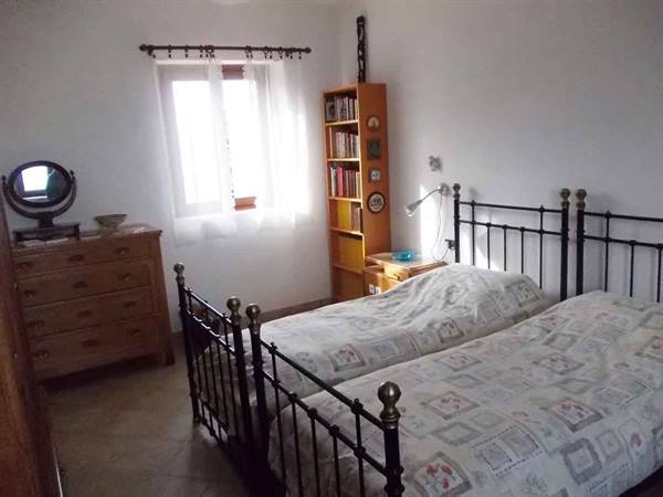 Bedroom with two wrought iron beds, wooden dresser and bookshelf by the window