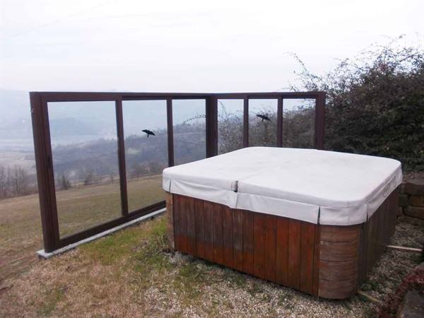 Wooden hot tub covered, on grassy terrace with glass wind screen