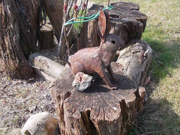 Rusty metal rabbit sculpture resting on a cut tree stump outdoors