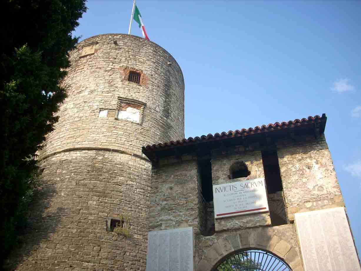Torre medievale in pietra con bandiera italiana accanto a portale con lapide marmorea