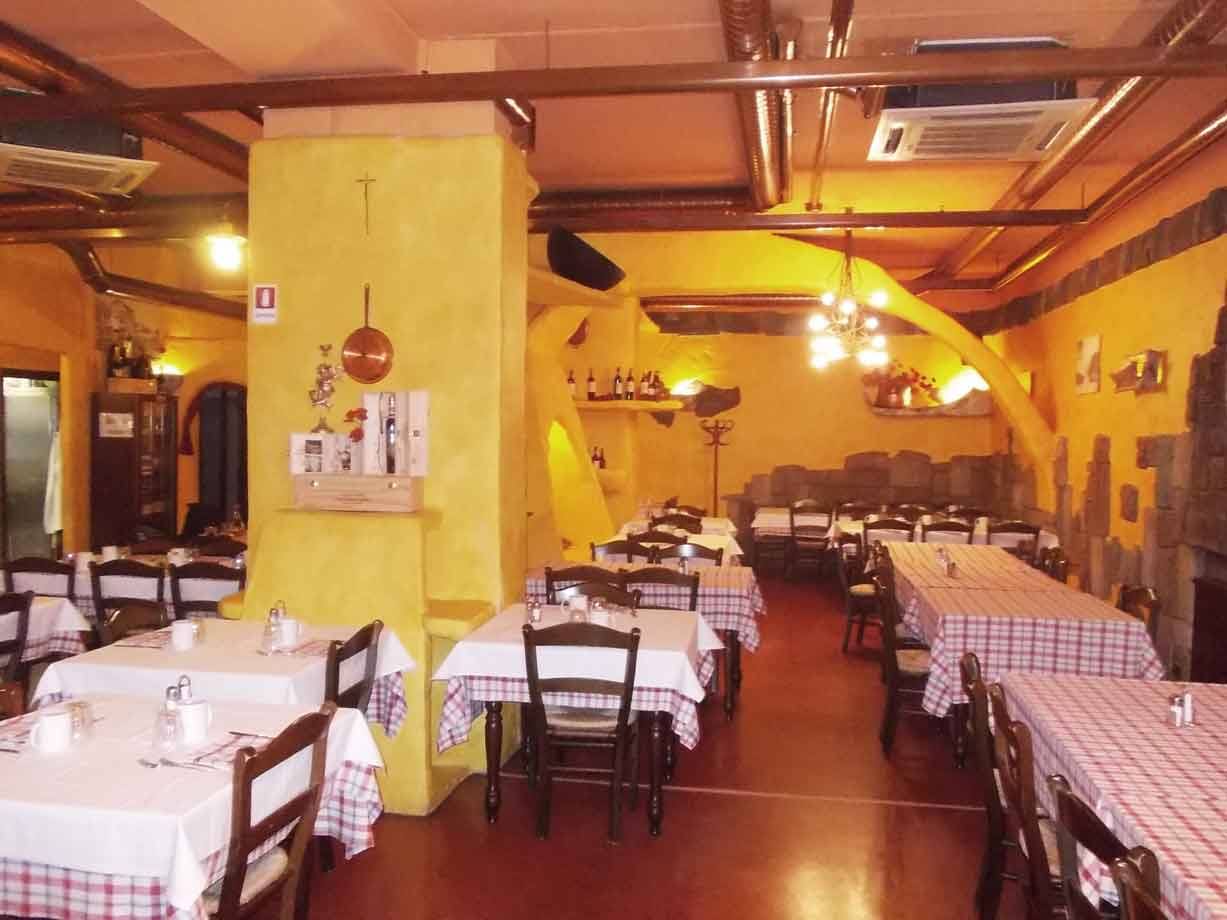 Sala di trattoria con tavoli apparecchiati, pareti gialle, travi in legno e lampadario
