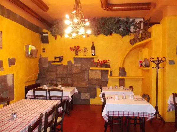 Trattoria dining room with yellow walls, stone, chandelier and checkered tablecloth tables