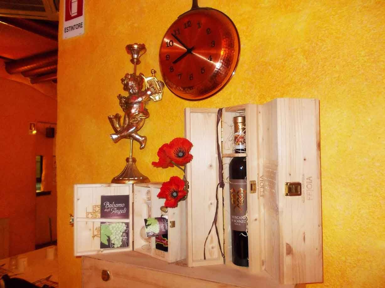 Bottiglia di vino in cassa di legno, orologio in rame e angelo dorato su parete gialla