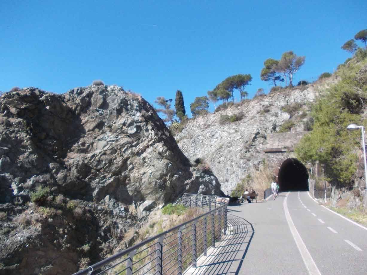 Ciclista entra nel tunnel scavatto nella roccia lungo la pista costiera assolata