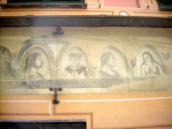 Faded fresco of female figures framed by arches, protected by glass on facade