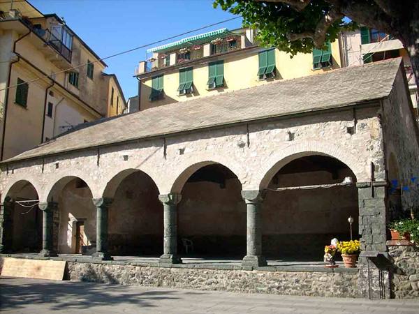Stone loggia with dark columns and arches among colorful houses in Vernazza